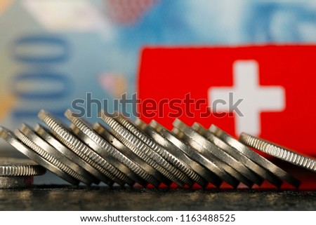 There are various Swiss coins visible against background of one hundred francs banknote and there is Swiss flag as well