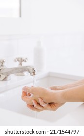 There Is Water Running In The Bathroom Sink While A Women Is Washing Her Hands. There Is A Label Free White Soap Dispenser In The Background. 