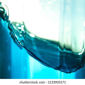 There Are The Waves And Splashes Of Azure Liquid In A Glass Container That Let Sunlight Through