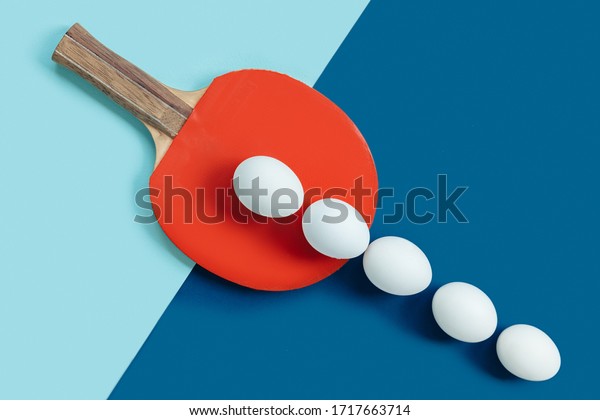 There are white eggs\
on the red table tennis racket. White eggs lie in a row and go out\
of bounds. The background of the image is divided into 2 parts by\
color and textures.