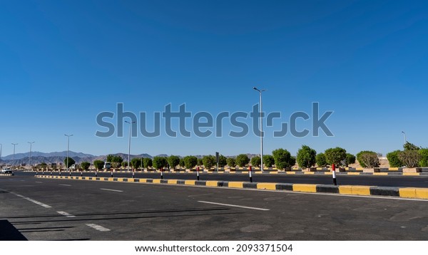 There are white marker lines on the paved highway.\
A black and yellow separation barrier in the middle. Green bushes\
on the side of the road. In the distance, against the blue sky -\
mountains. Egypt
