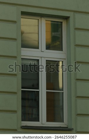 There is a white window located on the side of a greencolored building, creating a striking visual contrast in the architectural design