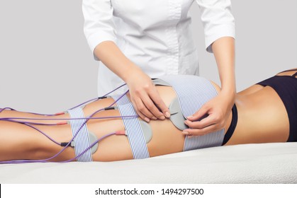 There is a woman, who is lying and is making anti cellulite procedure of myostimulation  on the legs and buttocks in a beauty salon. Caring for the body, reducing excess weight.
