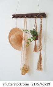 There Is A Wooden Hanger Hanging On The White Wall. On The Hanger There Are Decorative Elements Of A Straw Hat, A Wicker Bag With Lemons, A Wicker Planter With A Small Flower In A Pot.               