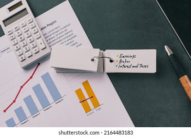 There is word card on the desk about Earnings Before Interest Taxes Depreciation and Amortization. It's placed with dummy documents.