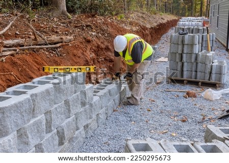 There was worker on construction site installing concrete block for retaining wall near new house that was being built