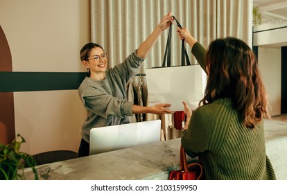 There you go. Friendly shop assistant handing a female customer a shopping bag with her clothing items. Happy store owner assisting an online shopper during an in store collection. - Shutterstock ID 2103159950