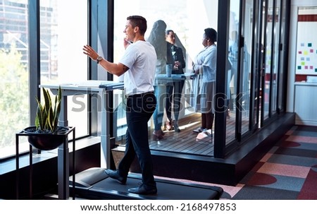 Theres no need to be deskbound as you head to success. Shot of a young businessman talking on a cellphone and going through paperwork while walking on a treadmill in an office.