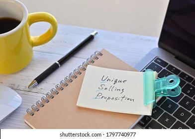 There's a note pinned to a clip on my desk. It says something like Unique Selling Proposition on it. There's a coffee and a pen and a laptop nearby. - Shutterstock ID 1797740977