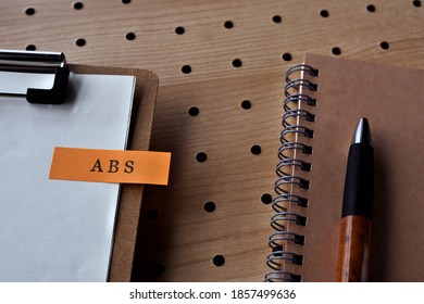 There's A Pen And A Notebook With A Sticky Note On It That Says ABS Written On It. It Was An Abbreviation For The Financial Term Asset Backed Security.