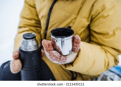 Thermo Mug In Hand. A Hand Holds A Mug Of Hot Tea. Drink Tea In The Winter Outside. A Metal Cup With A Drink Is Held By A Person. Tea From A Thermos. High Quality Photo