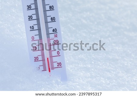 Thermometer with both Celsius and Fahrenheit scales placed in fresh snow indicating freezing cold winter temperature