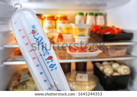 Thermometer in front of open fridge / refrigerator filled with food in kitchen