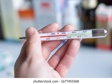 a thermometer with a high temperature in the hand against the background of medications