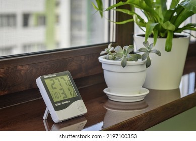 Thermometer hygrometer measuring the optimum temperature and humidity in a house on windowsill with houseplants closeup