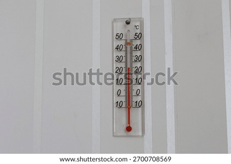 Thermometer on wall. With red marking or indicator. 25 degres celcius hot. Summer day.