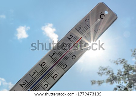 Thermometer shows heat in the summer season against a blue sky with sunbeams and lens flares, weather phenomenon due to climate warming with consequences like drought, forest fires and health hazards