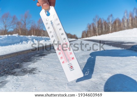 The thermometer shows a negative temperature in cold weather against the background of an icy road or highway.Poor weather conditions with low temperatures and ice.An icy snow-covered road or speedway