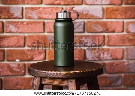 Thermos bottle near brick wall background. Coffee or tea reusable bottle container. Thermos travel tumbler. Insulated drink container.