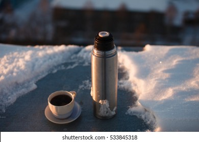 Thermos And A Cup Of Coffee In The Snow On The Roof.