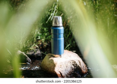 Thermos Outdoors. Vacuum Camping Flask Standing On A Stone In The Water.