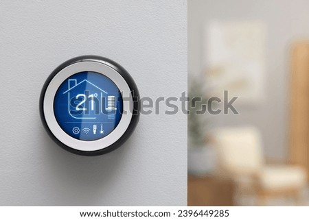 Thermostat displaying temperature in Celsius scale and different icons. Smart home device on white wall, space for text