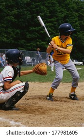 These Are Kids Playing In A Little League Baseball Game. It Shows Kids Playing Sports. There Is A Young Boy Up At Bat With The Catcher Situated Behind Him.