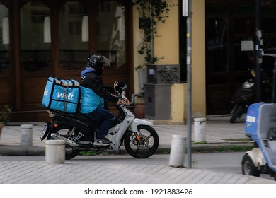 Thessaloniki, Greece - February 20 2021: Wolt Food Courier On Motorbike Speeding On City Road. Day View Of Male With Helmet Riding Motorcycle To Deliver Take Away Order Contained On A Company Logo Box