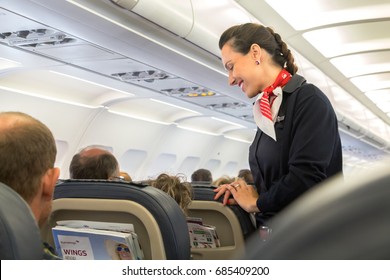 Thessaloniki , Greece - July 16, 2017: A Female Flight Attendant  Is Speaking With A Passenger Sitting In The Economy Class Of The Route Thessaloniki - Múnich Of Eurowings Airline.