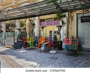 Thessaloniki, Greece - May 11 2020: Empty Outdoors Tables With Colorful Wooden Chairs Stacked Outside. Day View Of Tavern Chairs With Bright Colours Next To Closed Restaurants At Agiou Mina Street.