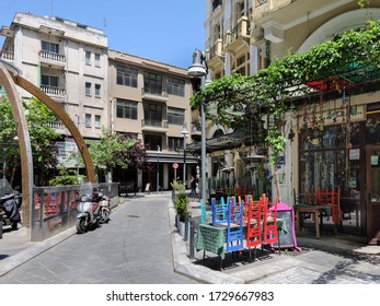 Thessaloniki, Greece - May 11 2020: Empty Outdoors Tables With Colorful Wooden Chairs Stacked Outside. Day View Of Tavern Chairs With Bright Colours Next To Closed Restaurants At Agiou Mina Street.