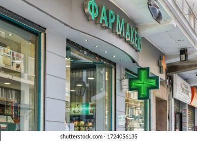 Thessaloniki, Greece May 4 - 2020: Greek open pharmacy store entrance with sign. External day view of Hellenic pharmaceutical shop with illuminated green cross.