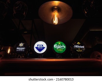 Thessaloniki, Greece - May 5 2022: Bar beer taps with various names and illuminated logos of brands including Fix Hellas, Carlsberg and Kaiser pilsner.