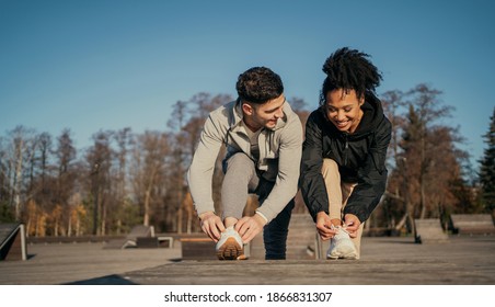 They adjust their white sneakers. a man and an African-American woman are engaged in active fitness sports on the street in the morning of a young couple. stretching aerobics in the city center - Powered by Shutterstock