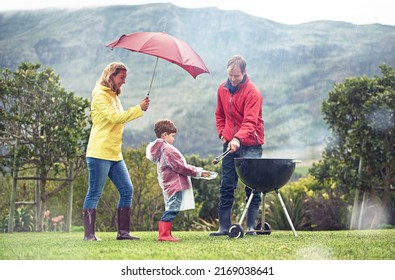 They Didnt Let A Little Rain Spoil Their Barbecue. Shot Of A Family Having A Barbecue Outside In Rainy Weather.