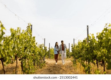 As they walk together, the couple enjoys the tranquility of the vineyards, surrounded by rows of green vines under a clear sky on a warm afternoon - Powered by Shutterstock