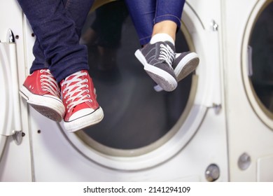 Theyre Relaxed While Doing Laundry. Cropped Image Of A Couples Feet As They Sit On A Washing Machine At The Laundromat.