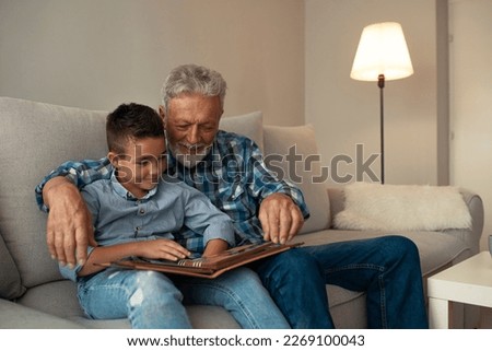 They've got a special bond. Happy family elderly man and little boy smiling r while sitting on couch and reading fascinating fairy tale together at home Photo stock © 