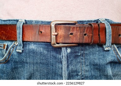 Thick brown belt on worn blue jeans, soft focus close up