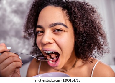 Thick Bushy Brows. Attractive Dark-haired Lady Throwing Chocolate Cereals In Her Open Mouth During Morning Mealtime