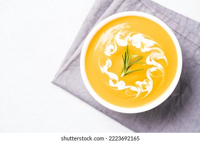 Thick Butternut Squash Bisque In White Bowl Garnished With Heavy Cream And Rosemary Over White Table. Bowl Of Pumpkin Cream Soup. View Overhead. Minimal Style. Selective Focus