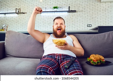 Thick Funny Man In Pajamas Eating A Burger Sitting On The Couch.