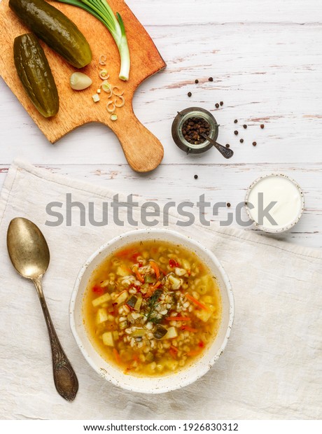 Thick hearty Pickle soup with vegetables\
(pickles, cucumbers, carrots, onions, potatoes, tomatoes, dill) and\
pearl barley in a white plate on a wooden table. Rassolnik. Dish of\
Russian cuisine