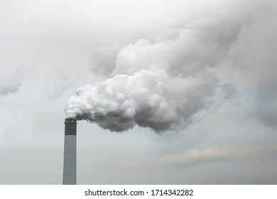 Thick and heavy smoke coming out of a huge and high chemical factory chimney under a misty and rainy sky