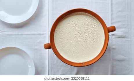 Thick homemade Bulgarian yoghurt in a ceramic pot on a white tablecloth with white plates. Organic healthy food. Natural probiotic.  - Shutterstock ID 2320068111
