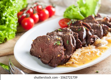 Thick juicy portions of grilled hanger beef fillet steak with orange sauce served with tomatoes lettuce salad and thyme on old wooden table