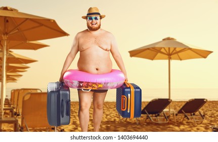 Thick man in a swimsuit with a suitcase and a rubber ring against the background of a summer beach.