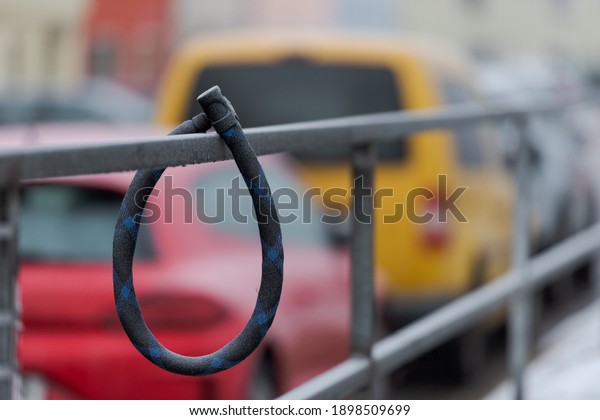 Thick round\
bike lock covered in white frost hanging on metal handrail in city\
with cars in background without\
bike