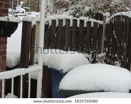Thick snow on top of wheelie bins near the front of a house