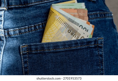 Thick stack of euro banknotes including different denominations protruding from blue denim jeans pocket with white studded belt. Concept of money saving, cash payments and budget management. 